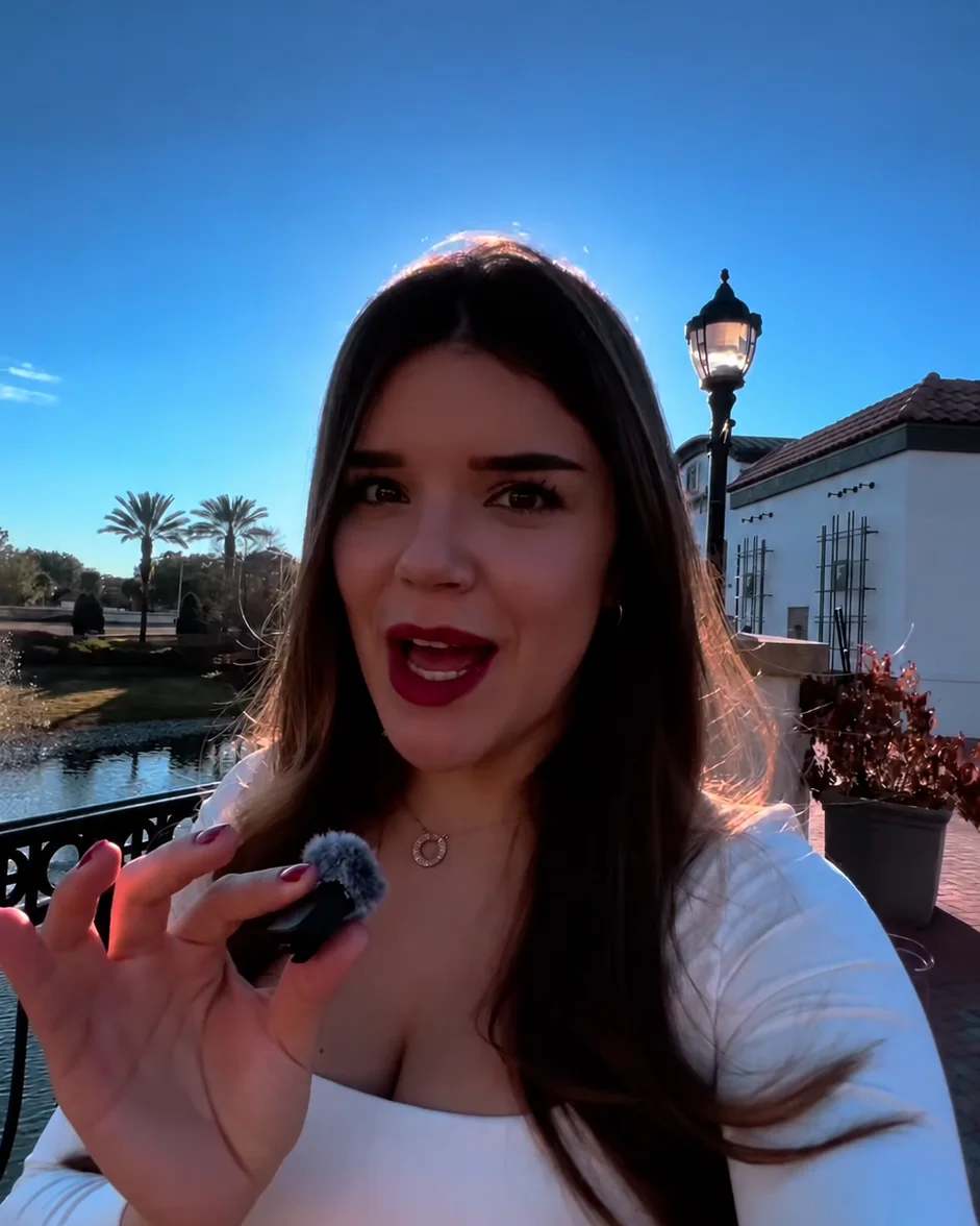 Anna Gouveia gravando conteúdo ao ar livre na Flórida, com palmeiras e um lago ao fundo
